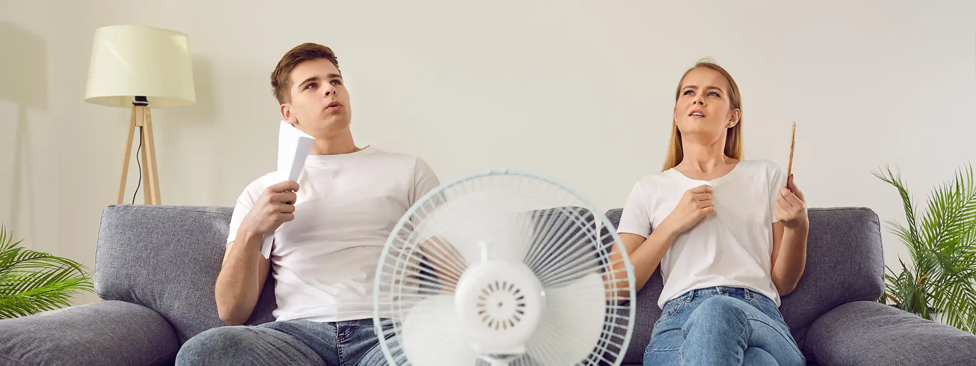 A young couple in a home without air conditioning sitting in front of a fan