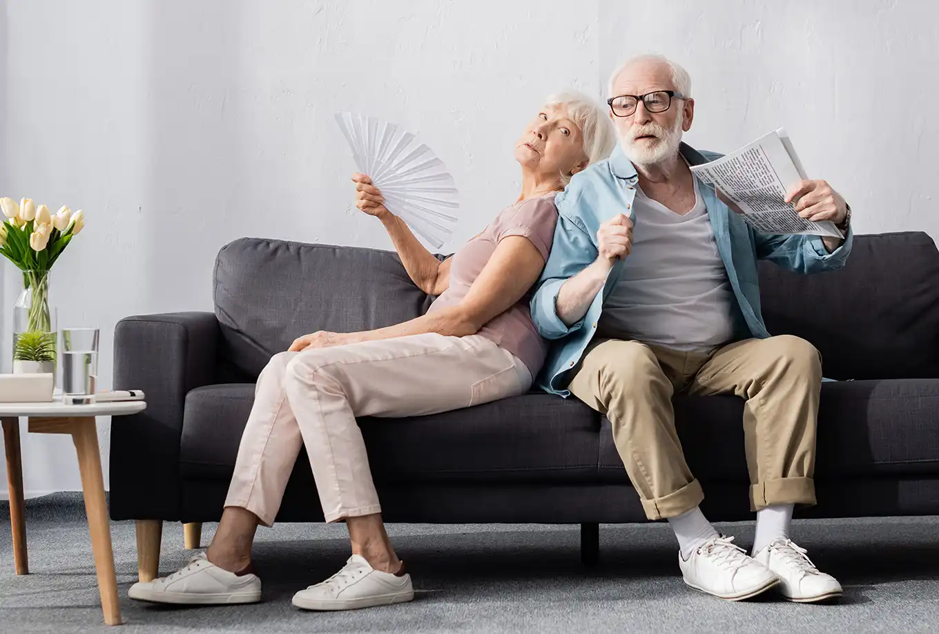 A older couple fanning themselves in their home with the AC unit not working