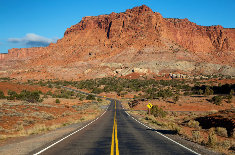Scenic view of an open desert highway leading toward red rock mountains, highlighting nearby outdoor recreation and travel.