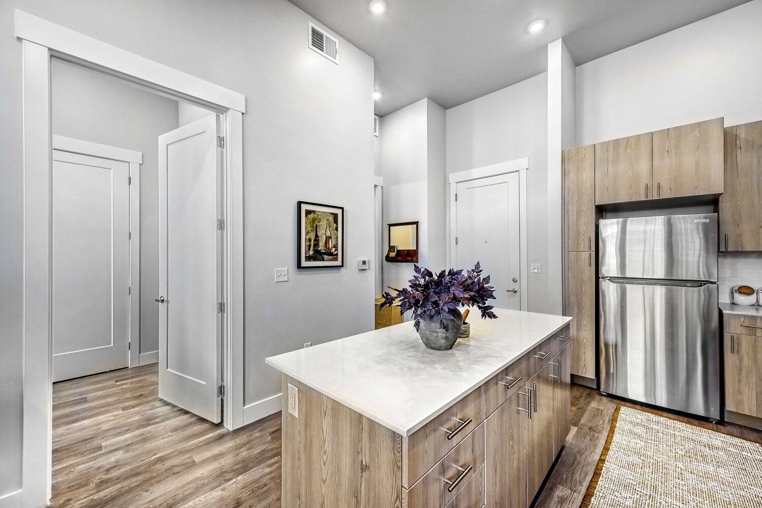 Open-concept entryway and kitchen area showing light hardwood-style flooring, high ceilings, and a large kitchen prep island.