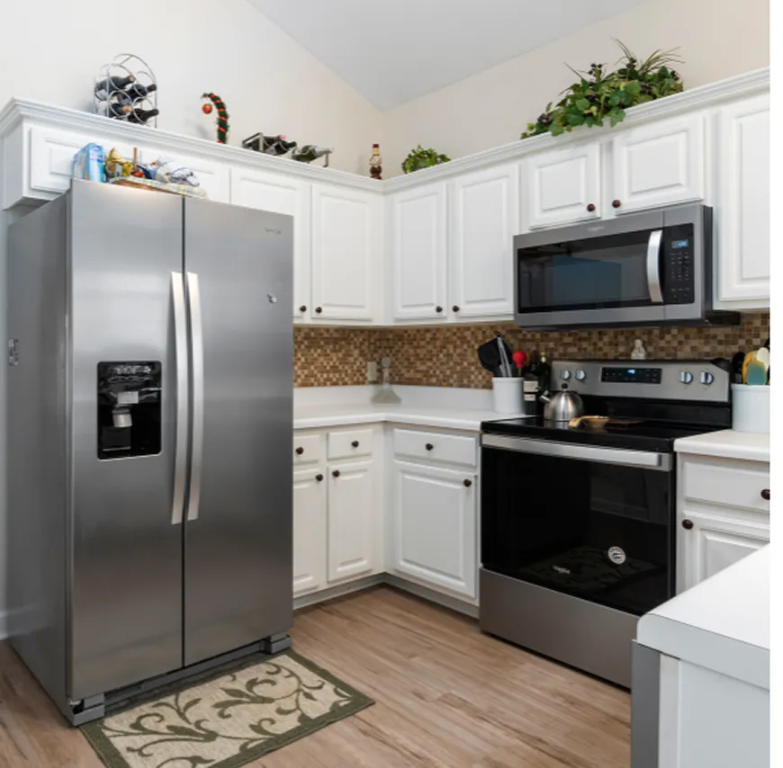 Modern kitchen corner with stainless steel refrigerator, oven with stove, microwave, white cabinets, and patterned backsplash.