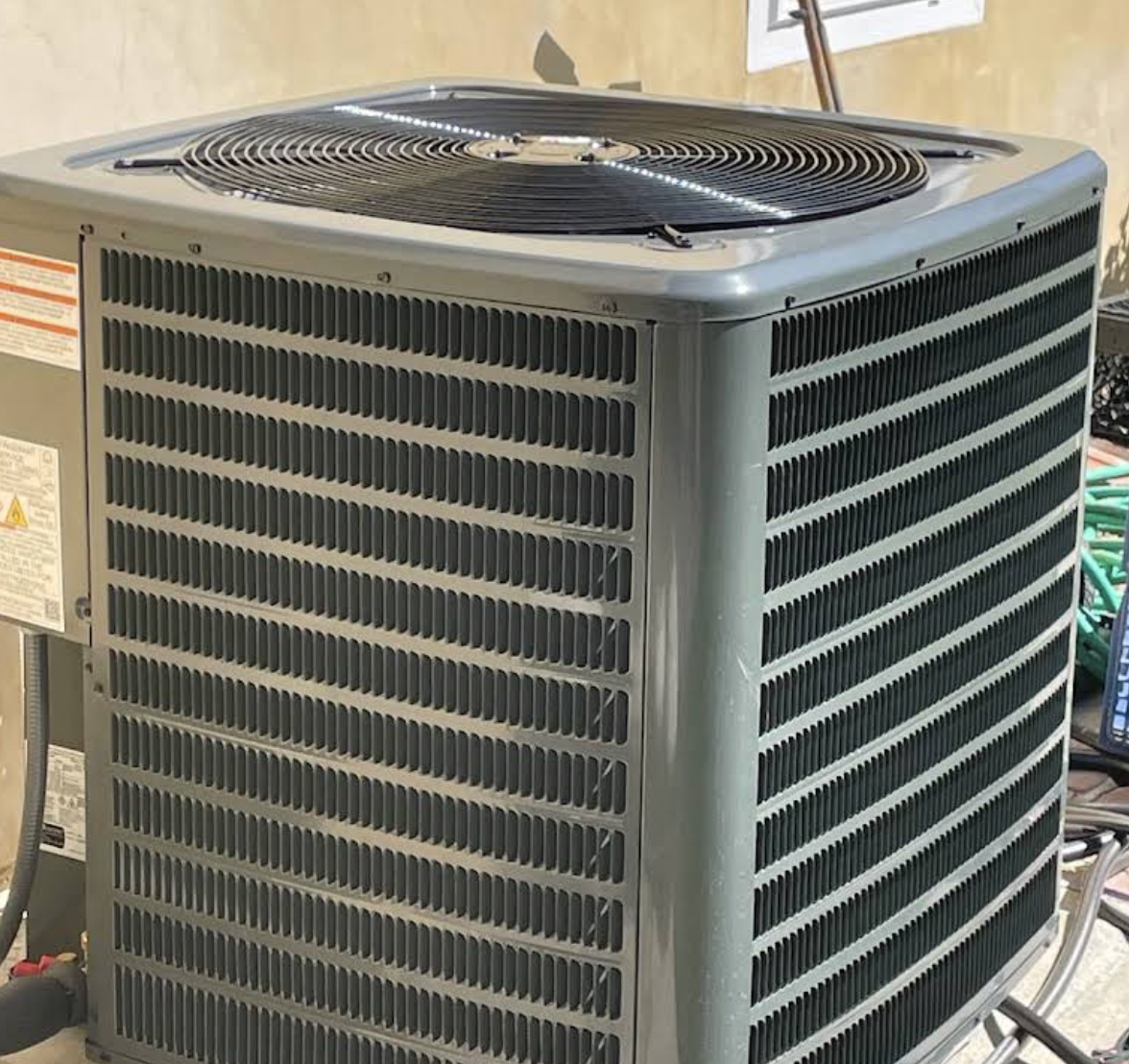 Outdoor central air conditioning unit with metal grille and top fan in a residential area.