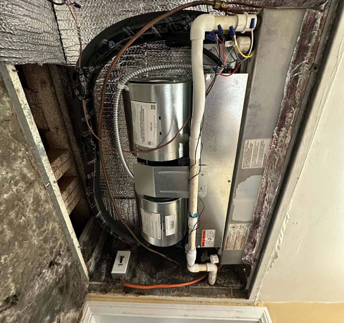 Metal HVAC system with insulated pipes, wiring, and PVC drain tubing in a utility closet.