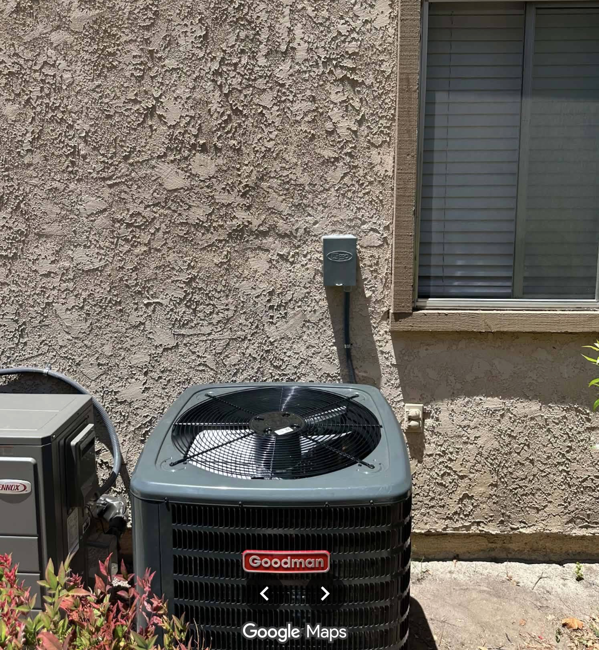 Goodman air conditioning unit and a Lennox unit outside a textured beige stucco house wall with a window.