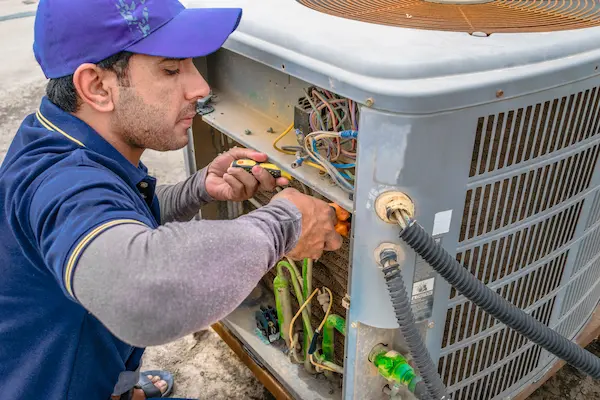 Technician repairing or inspecting an outdoor HVAC unit with tools in hand.