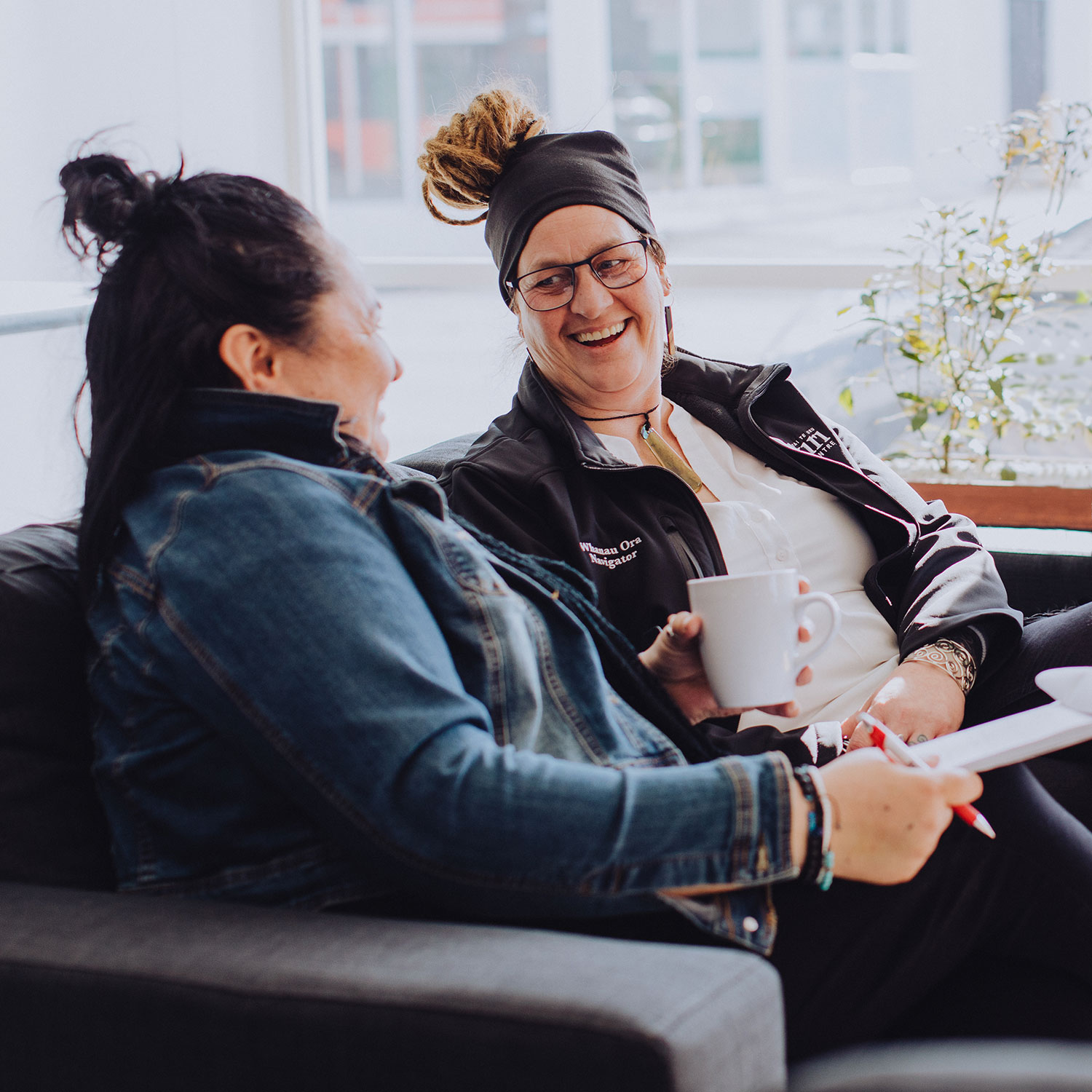 Two women sitting on a couch looking at each other and smiling