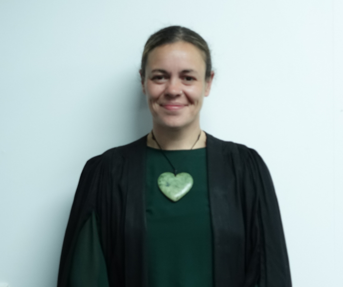 Woman smiling wearing a dark robe and a green heart-shaped pendant necklace.