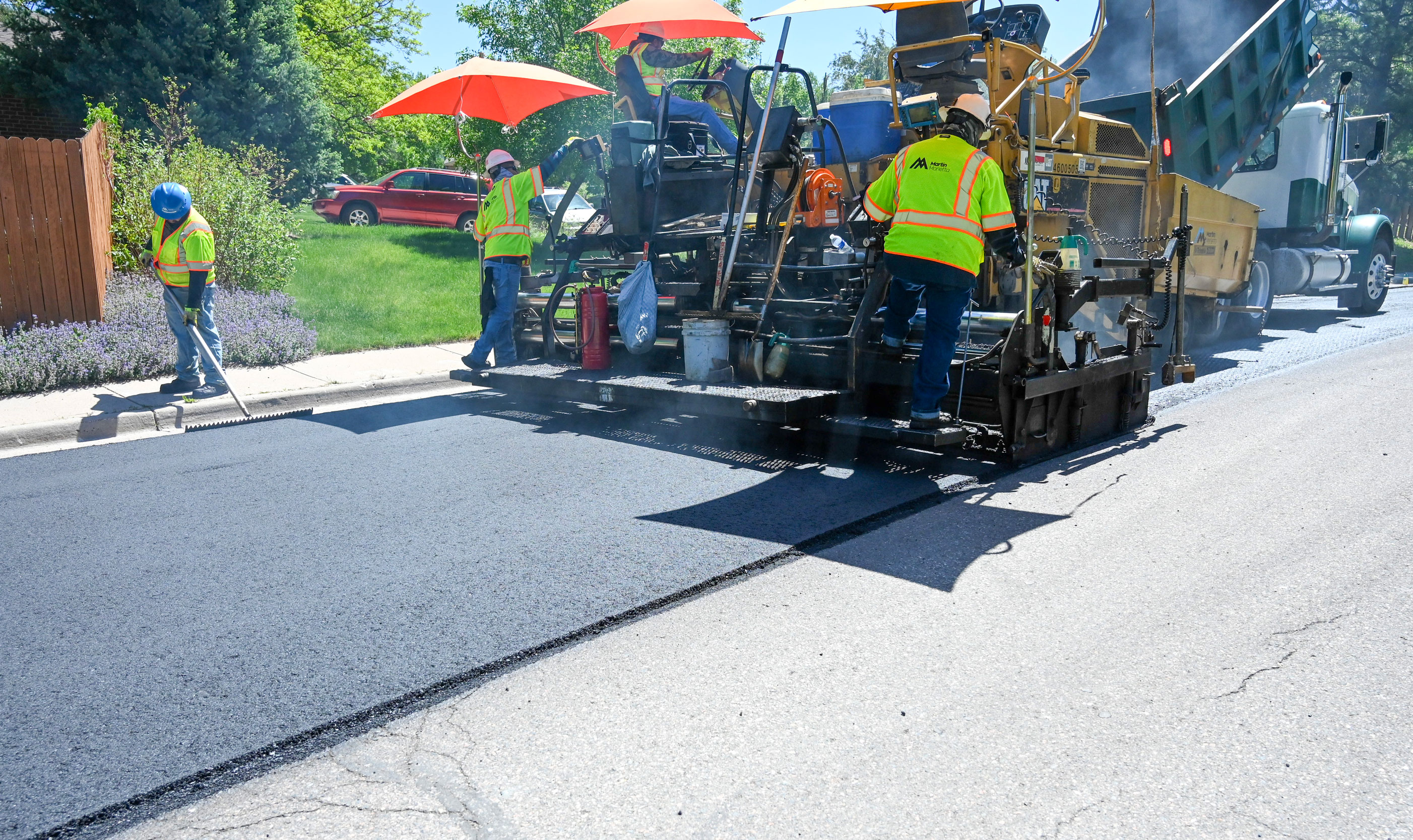 Workers in safety vests paving a street with asphalt using heavy machinery on a sunny day.