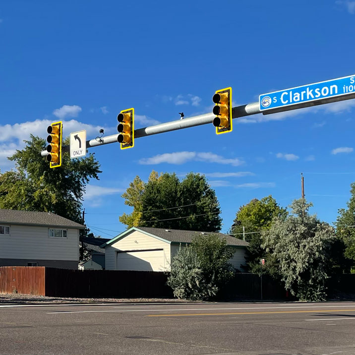 Traffic lights at an intersection with a street sign for S Clarkson St against a clear blue sky.
