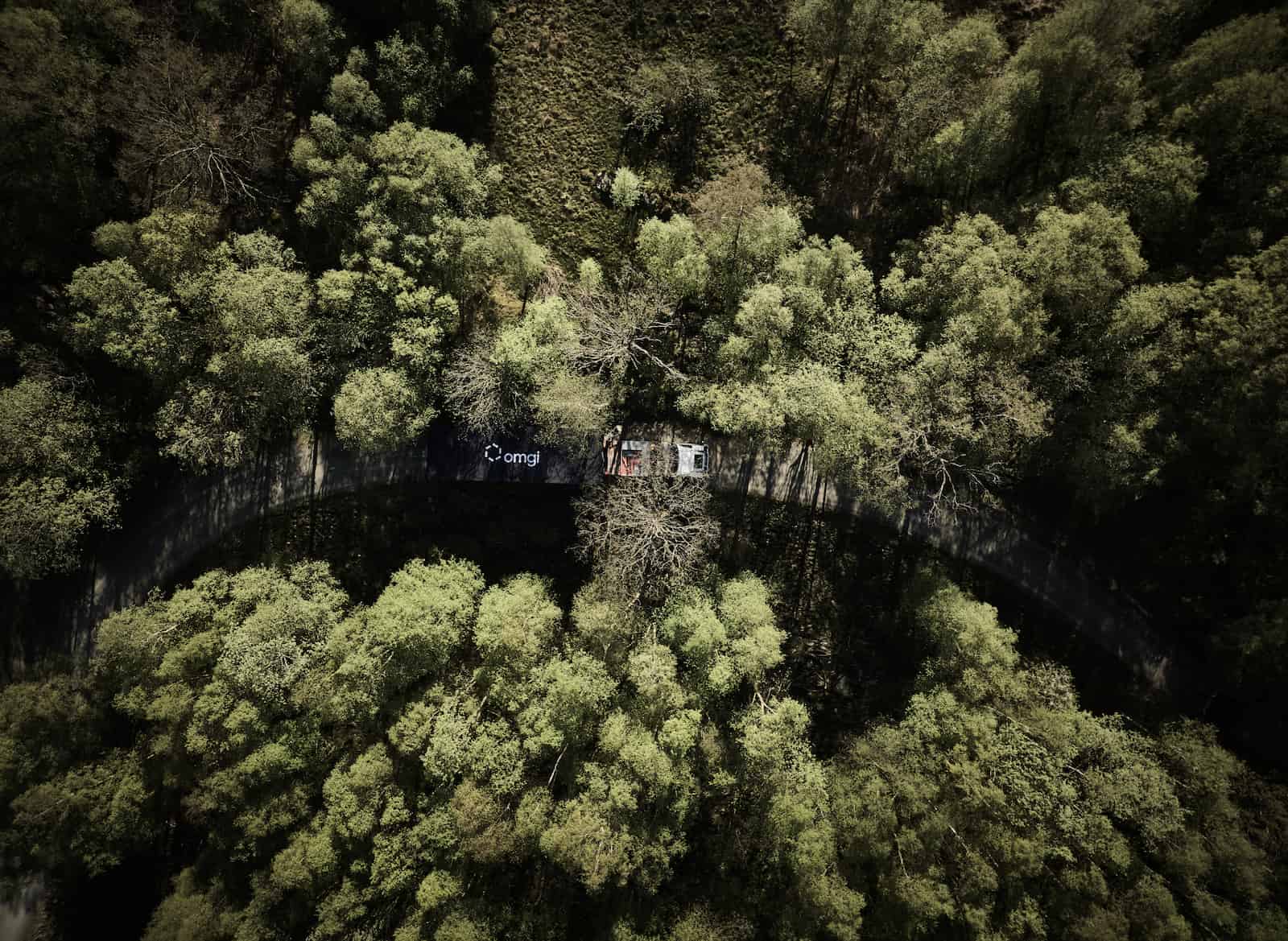 En lastebil med Omgi på hengeren kjører gjennom grønn skog, sett fra fugleperspektiv