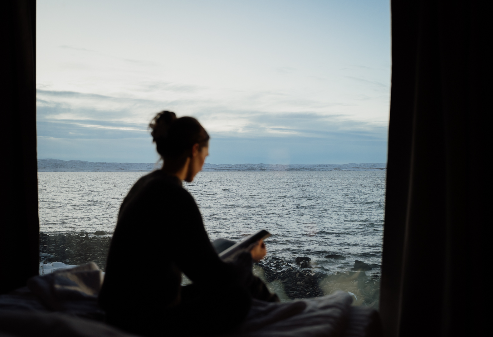 Damer leser på seng i forgrunnen. Hav bak.