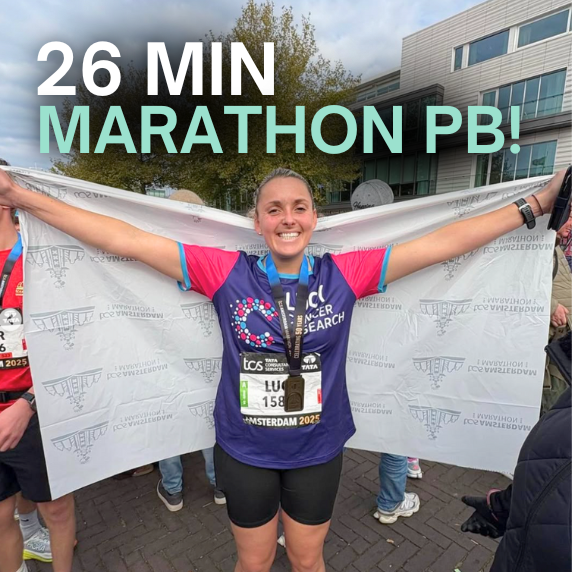 Smiling female runner holding a white banner with arms outstretched, wearing a medal and race bib after a marathon, with text '26 MIN MARATHON PB!' above.