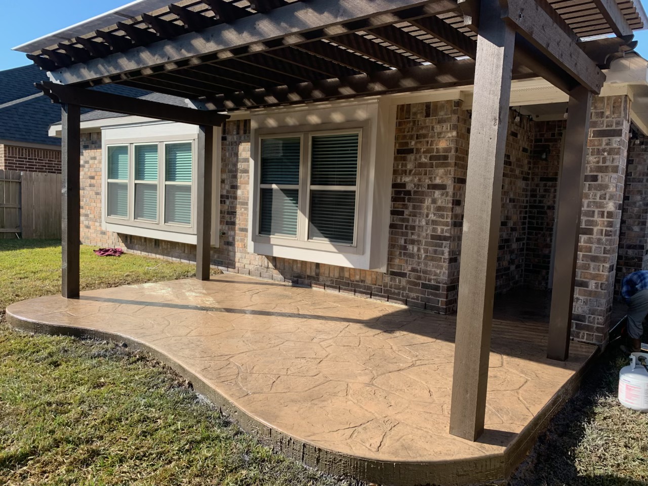 A new pergola with a stone-like patio surface installed over the backyard of a b