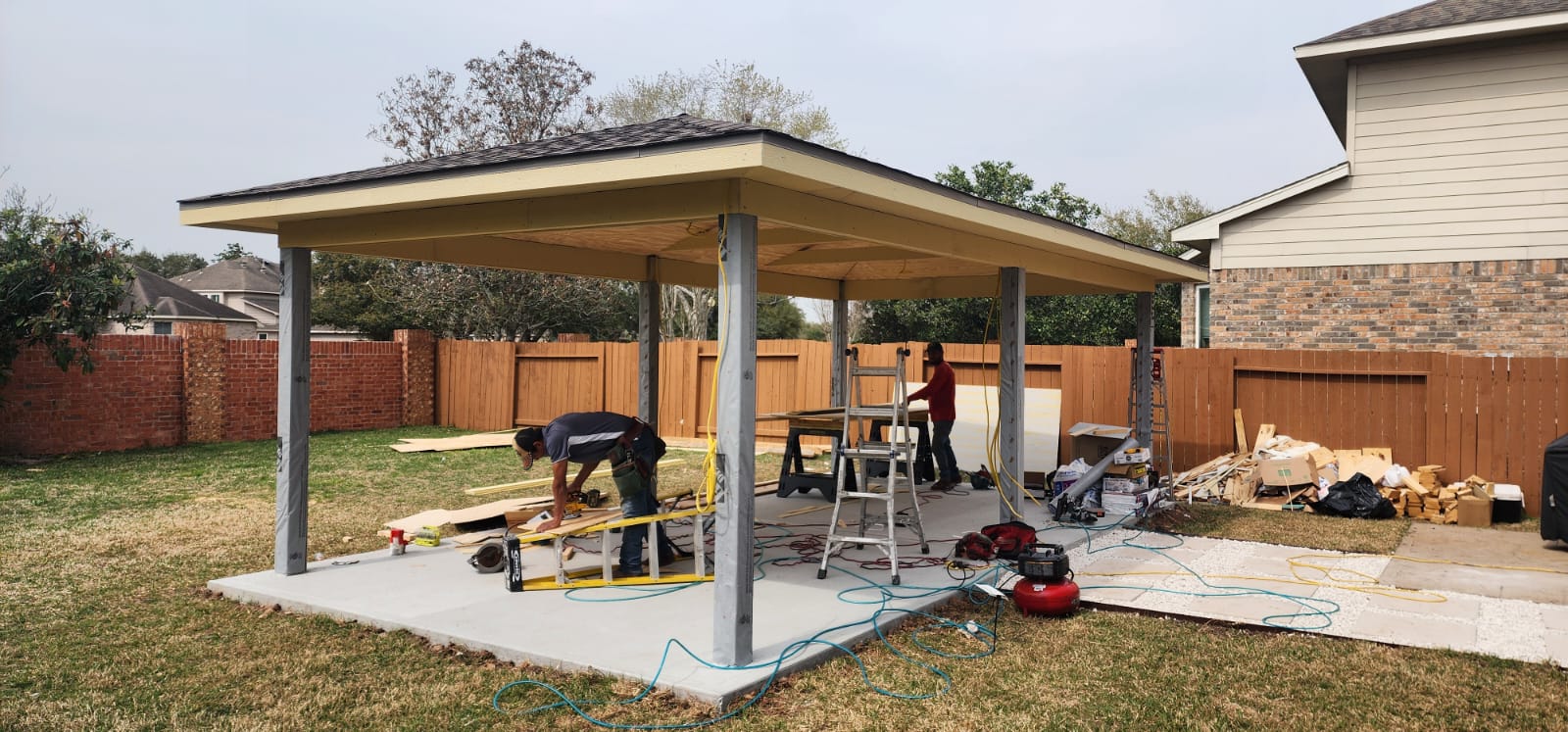 Two workers are building a pergola in a backyard.