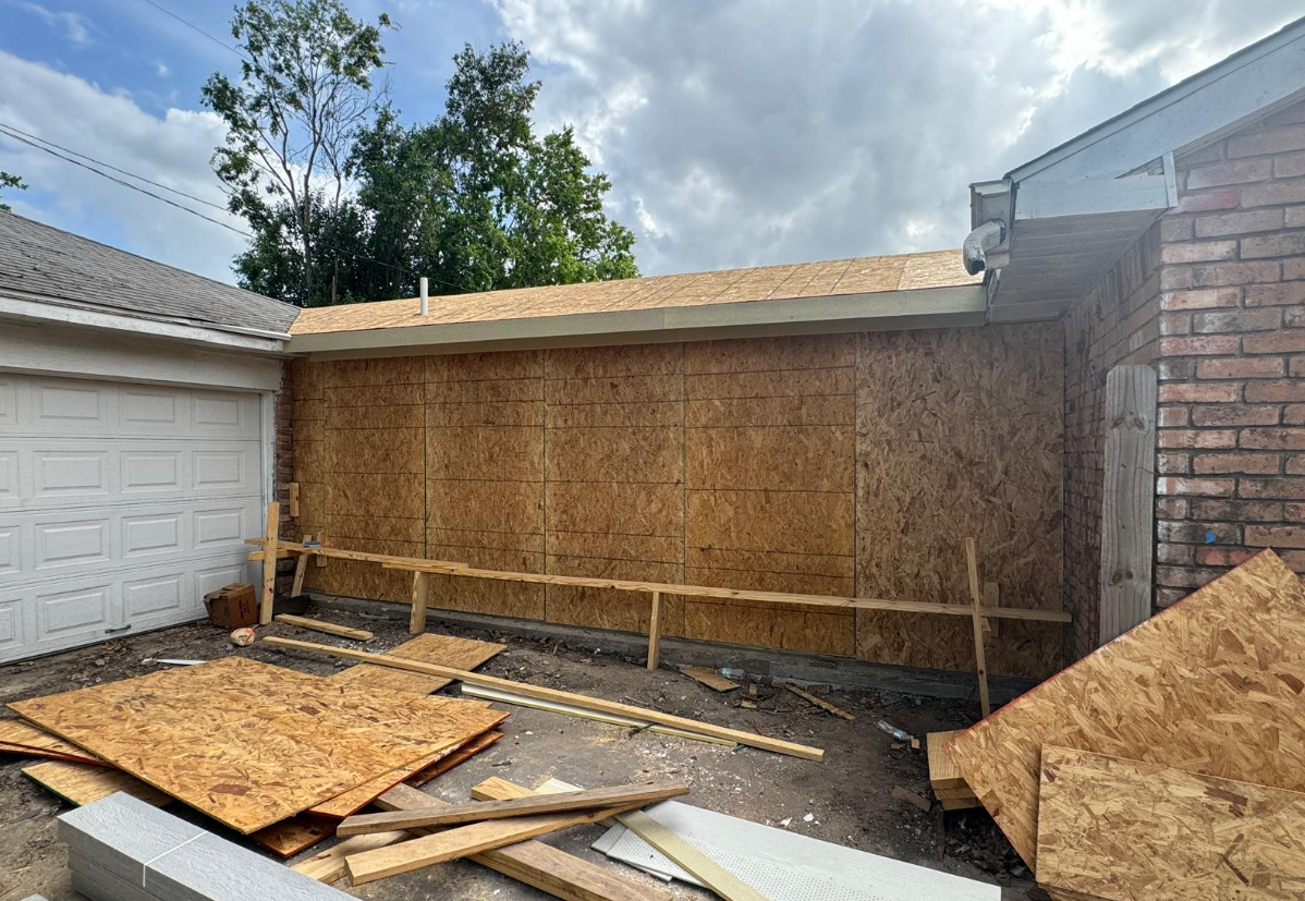 An outdoor construction site featuring a building being renovated with newly installed OSB sheathing on the walls and roof. —