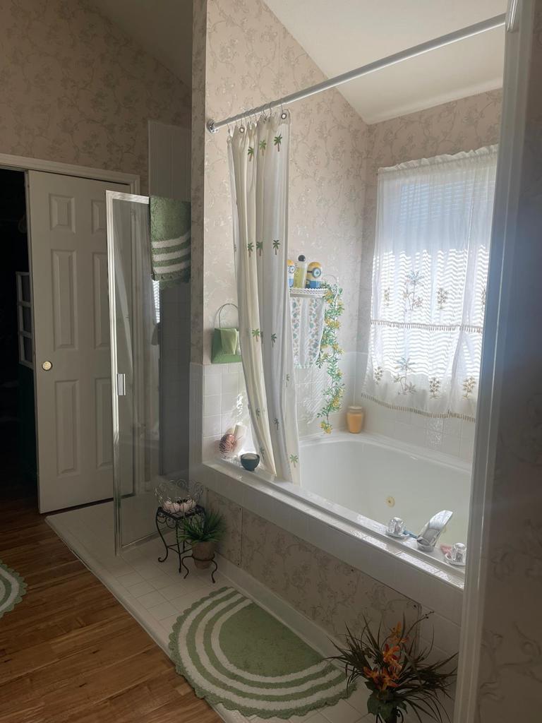A bathroom featuring a large white bathtub with a patterned shower curtain, a glass shower enclosure, and floral wallpaper. —