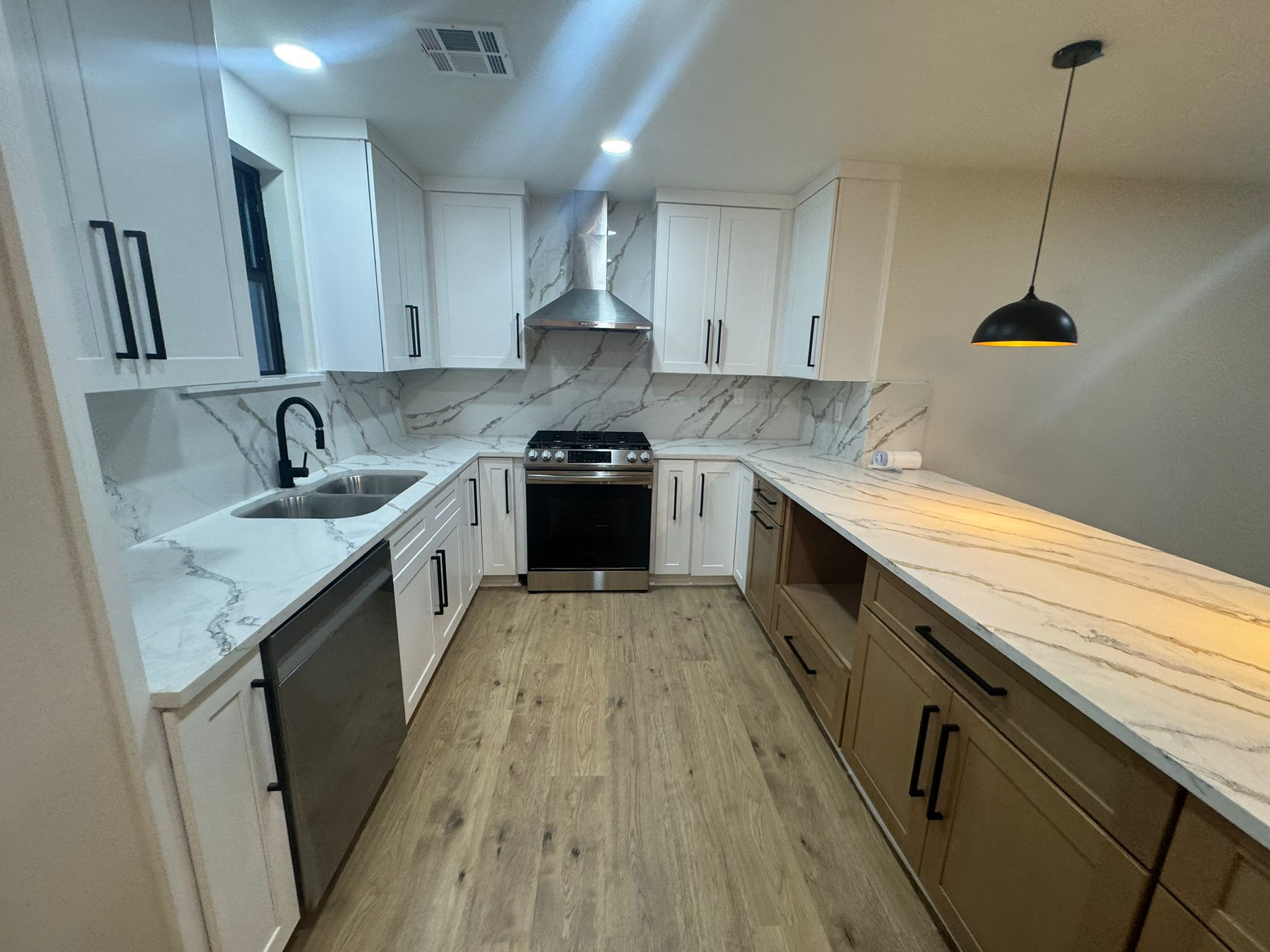 A modern kitchen featuring white cabinetry, marble-patterned countertops, light wood floors, and stainless steel appliances.