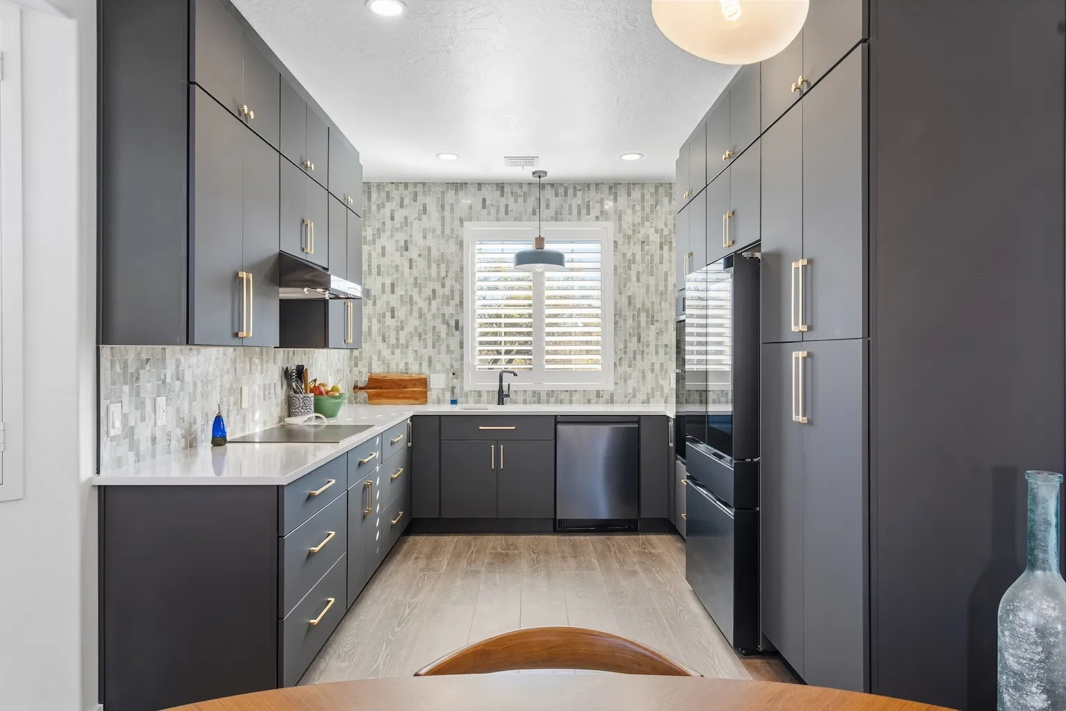 Modern kitchen with dark gray cabinets, white countertops, mosaic tile backsplash, and stainless steel appliances.