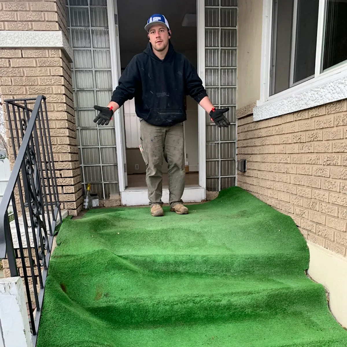 Man standing at a house entrance with wrinkled green outdoor carpet covering the steps.