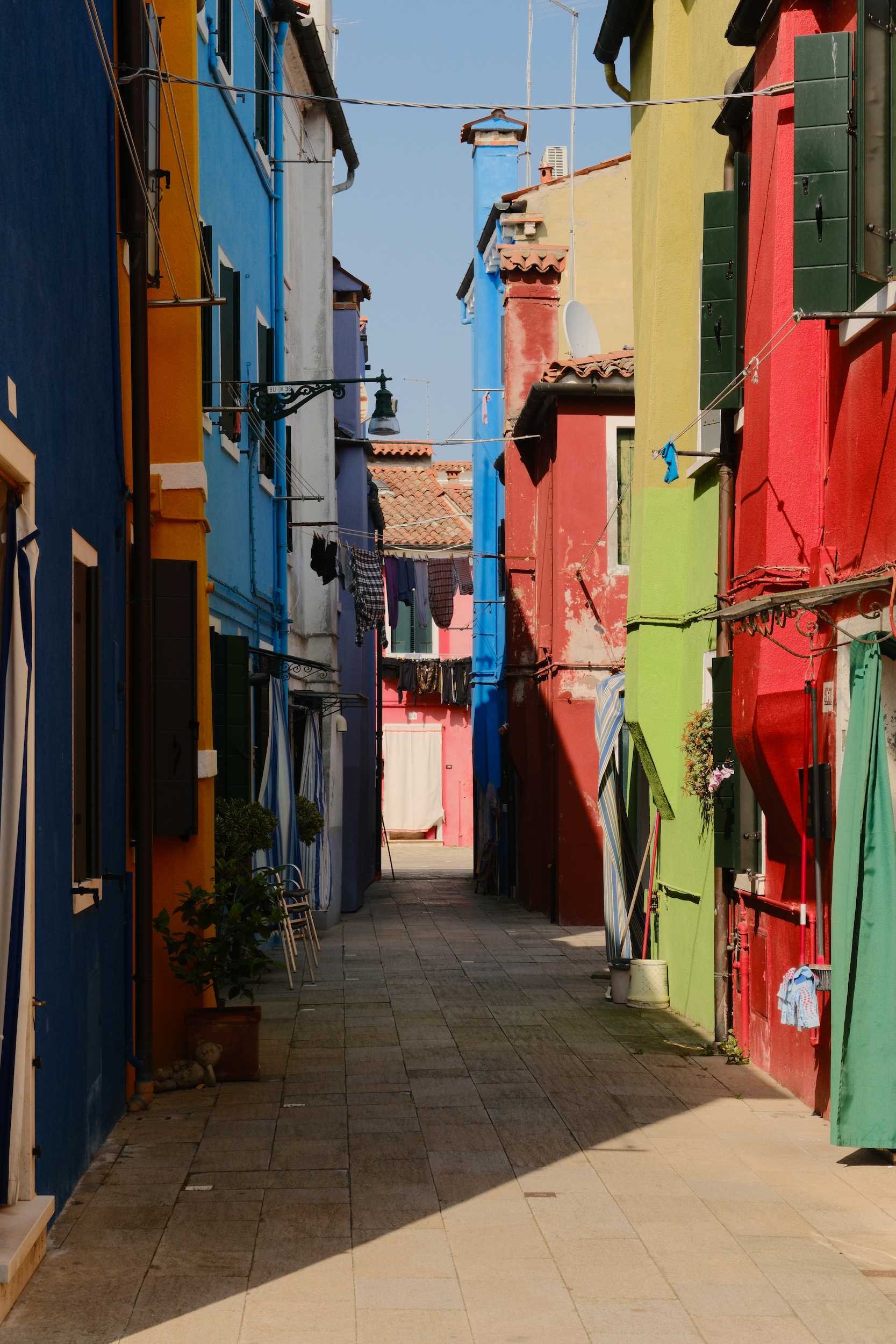 Narrow alley lined with brightly colored buildings in shades of red, green, blue, yellow, and purple with clothes hanging on lines.