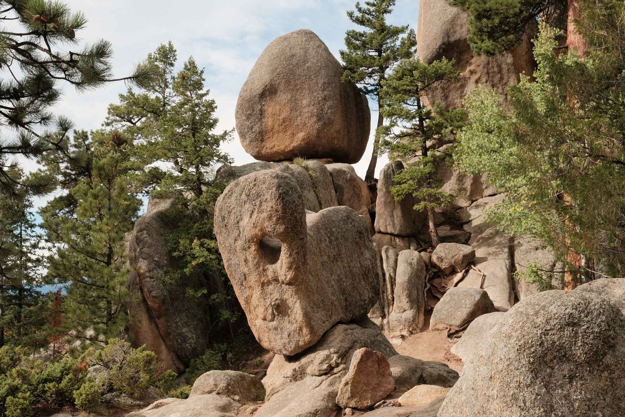 Large balanced boulders surrounded by pine trees in a rocky forested landscape.