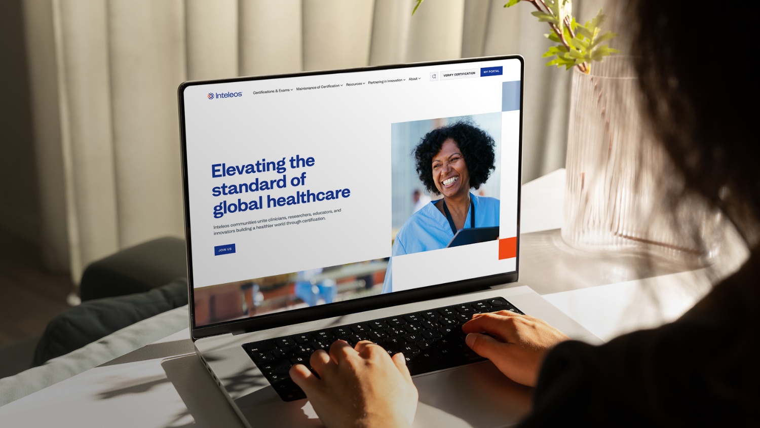 Person typing on a laptop displaying a healthcare website with the headline 'Elevating the standard of global healthcare' and a smiling healthcare worker.