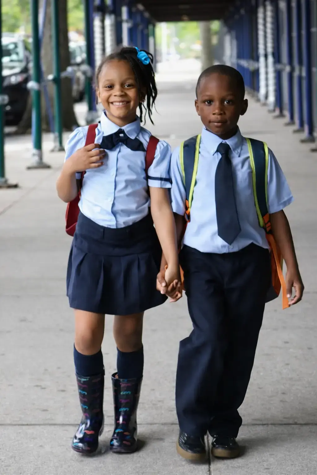 Two young students in school uniforms holding hands with backpacks