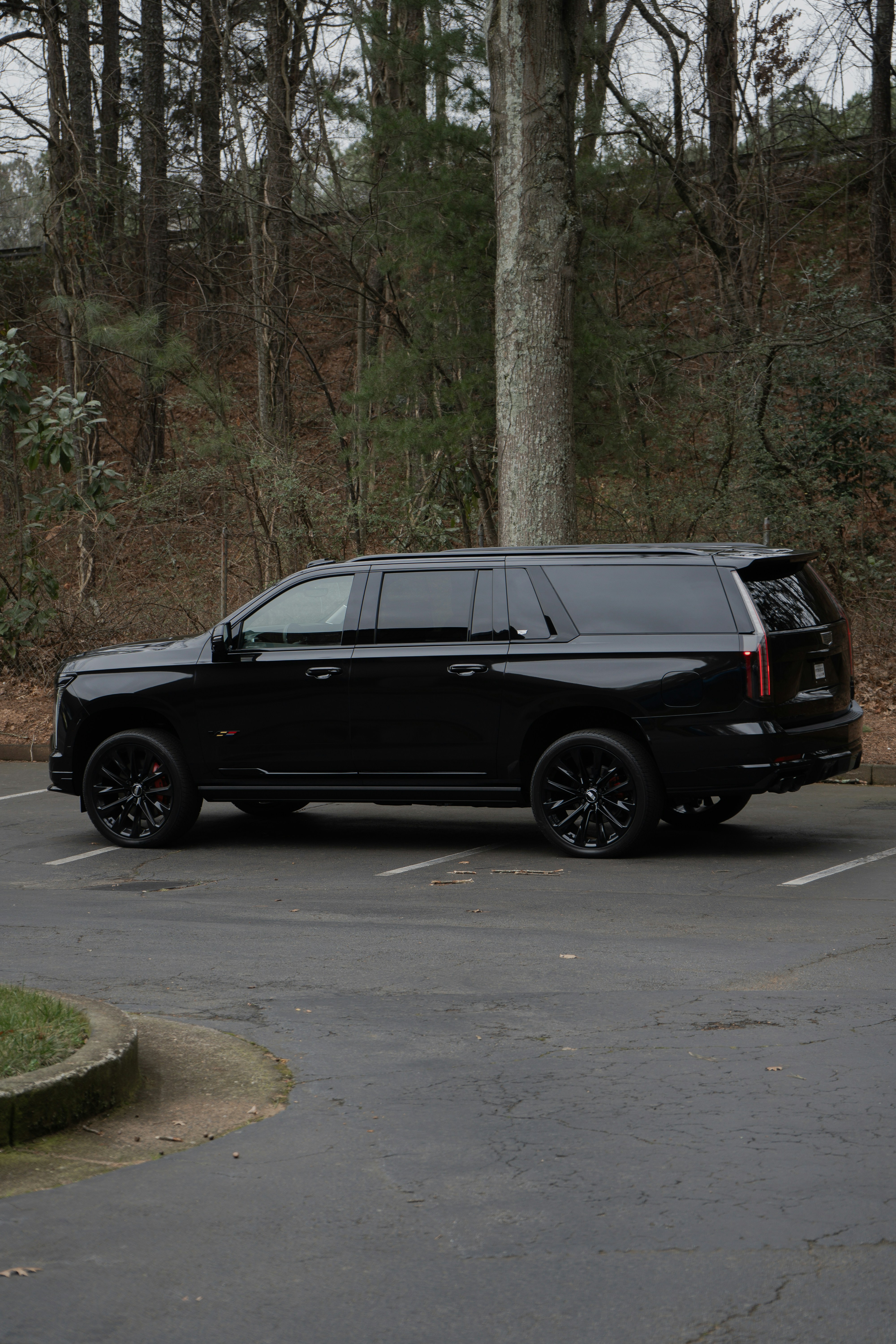 Black luxury SUV parked in a lot with trees and a wooded area in the background.