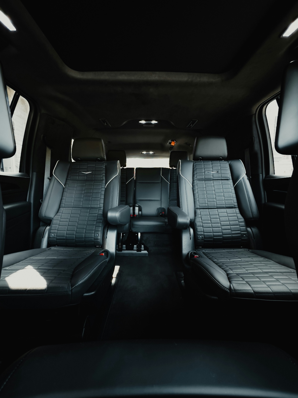 Interior view of a vehicle with black leather captain seats and rear bench seating.