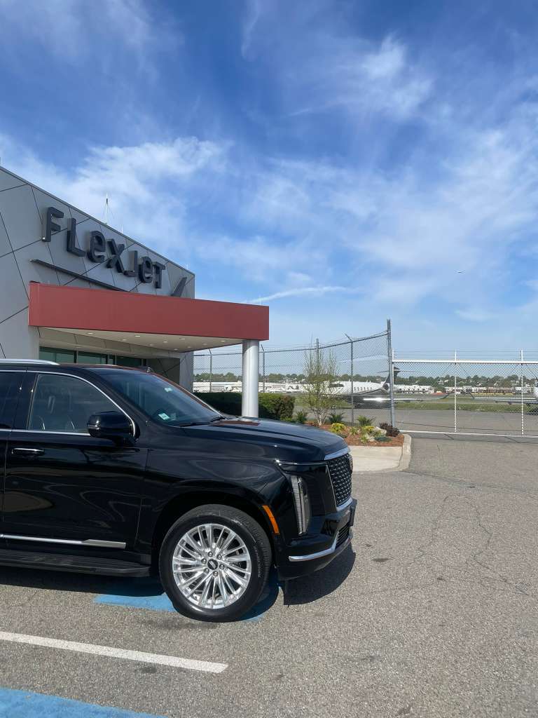 Black luxury SUV parked outside a building with Flexjet signage under blue sky.