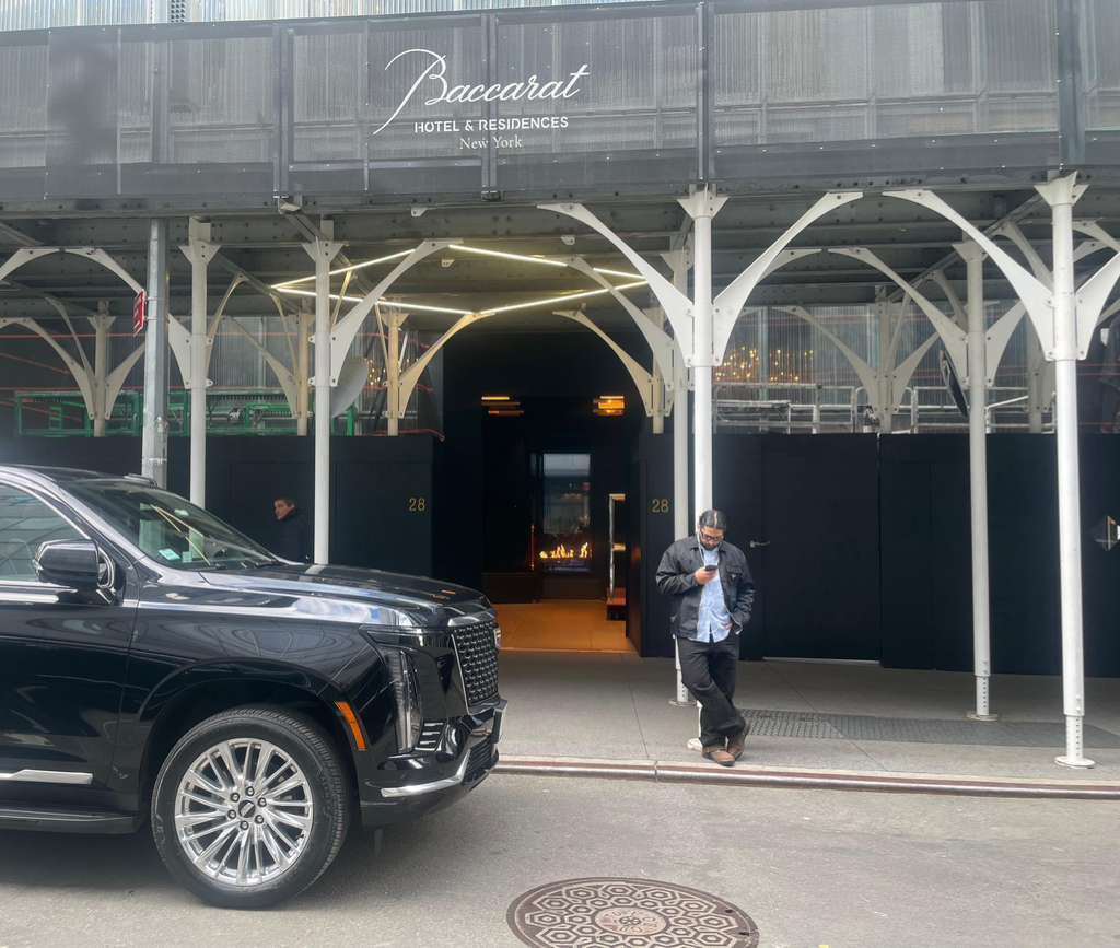 Entrance of Baccarat Hotel & Residences New York with a black SUV and a man looking at his phone.