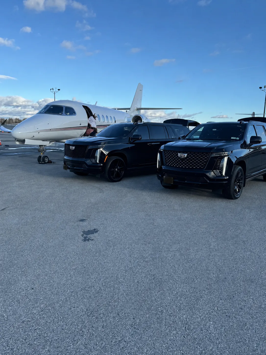 Two GeronimoLux Cadillac Escalades parked on the tarmac beside private jets for a private aviation pickup