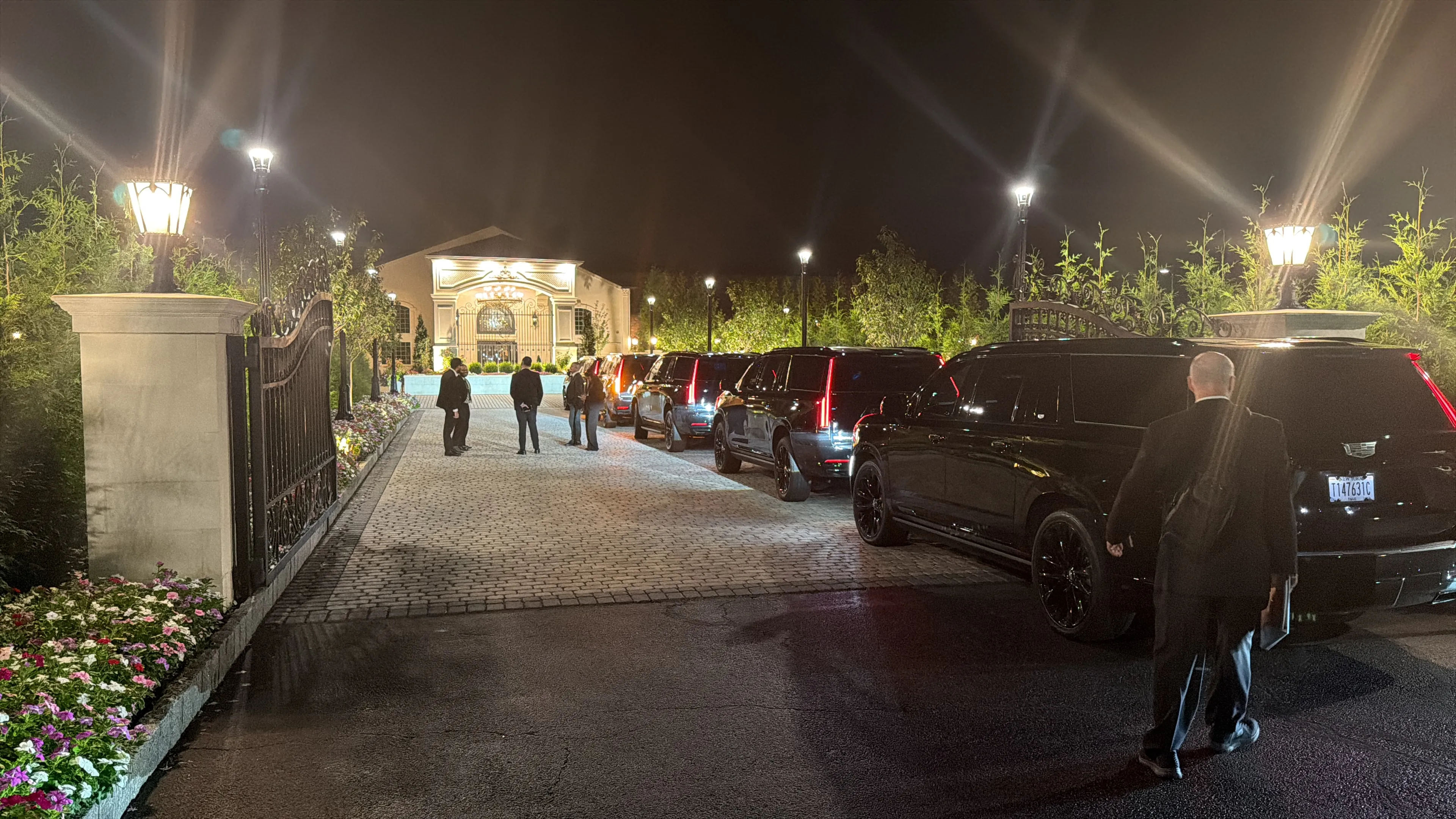 GeronimoLux fleet of black SUVs lined up at night outside a wedding venue, with a chauffeur waiting for the couple and guests
