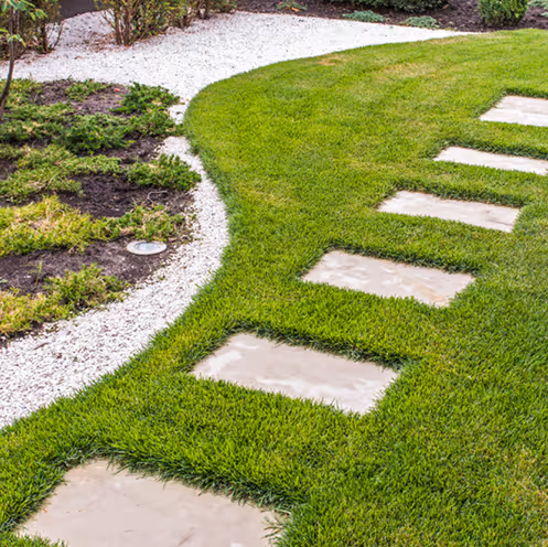 Curved garden path with rectangular stepping stones embedded in green grass next to gravel and plants.