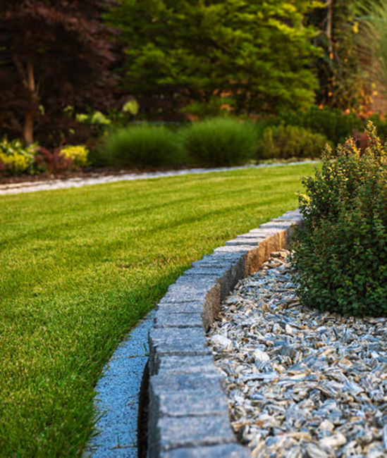 Curved stone edging separating green lawn and landscaped area with small shrubs and decorative rocks.
