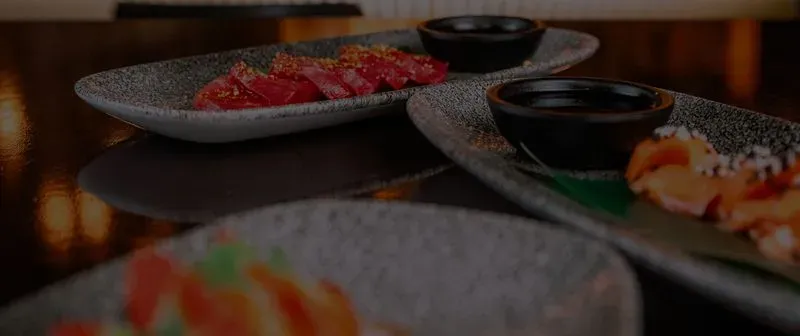 Three rectangular plates with sushi and dipping bowls on a dark table.