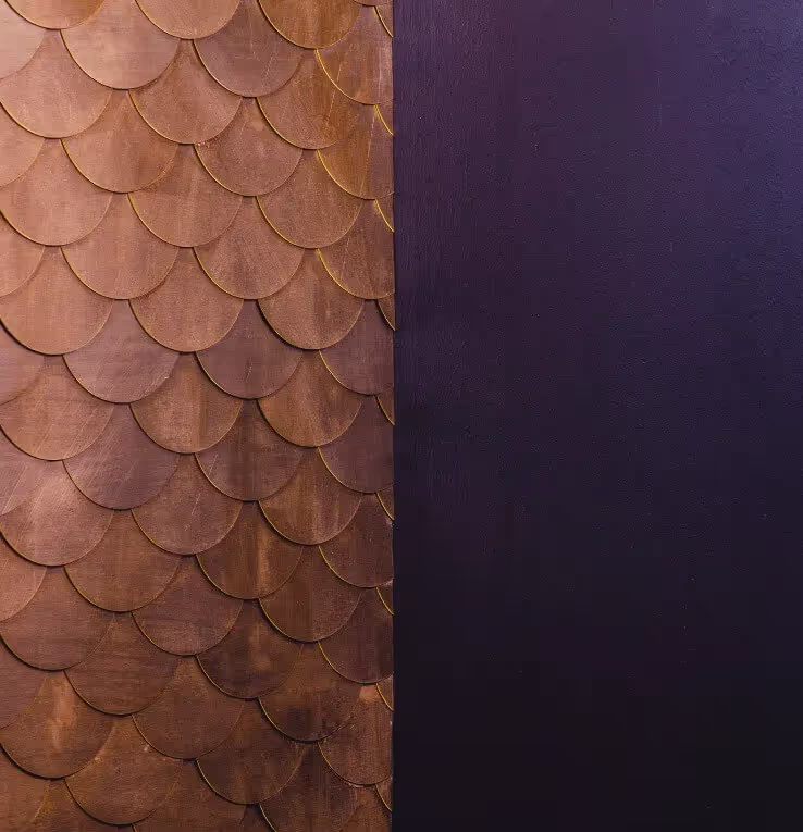 Wall with brown scalloped wooden tiles on the left half and smooth dark purple surface on the right half.