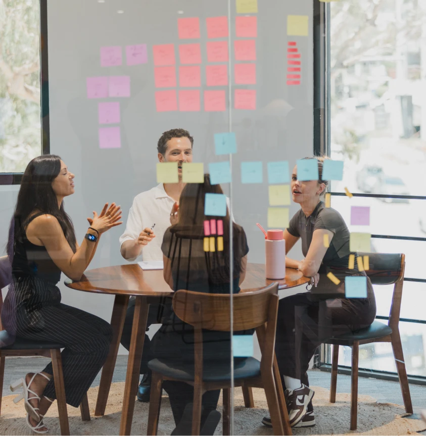 Team of four at a meeting, brainstorming with sticky notes on a glass wall, business collaboration.