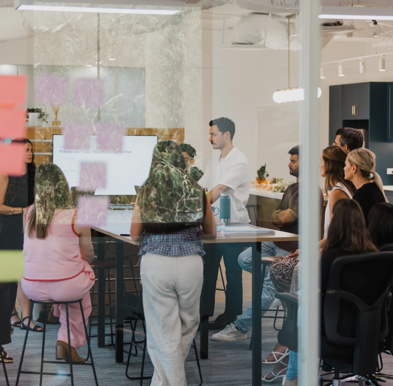 Business meeting in modern office, people around conference table. Presentation screen visible, brainstorming session.