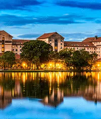 Lake with illuminated buildings, trees reflecting in water at dusk. Cityscape night view.