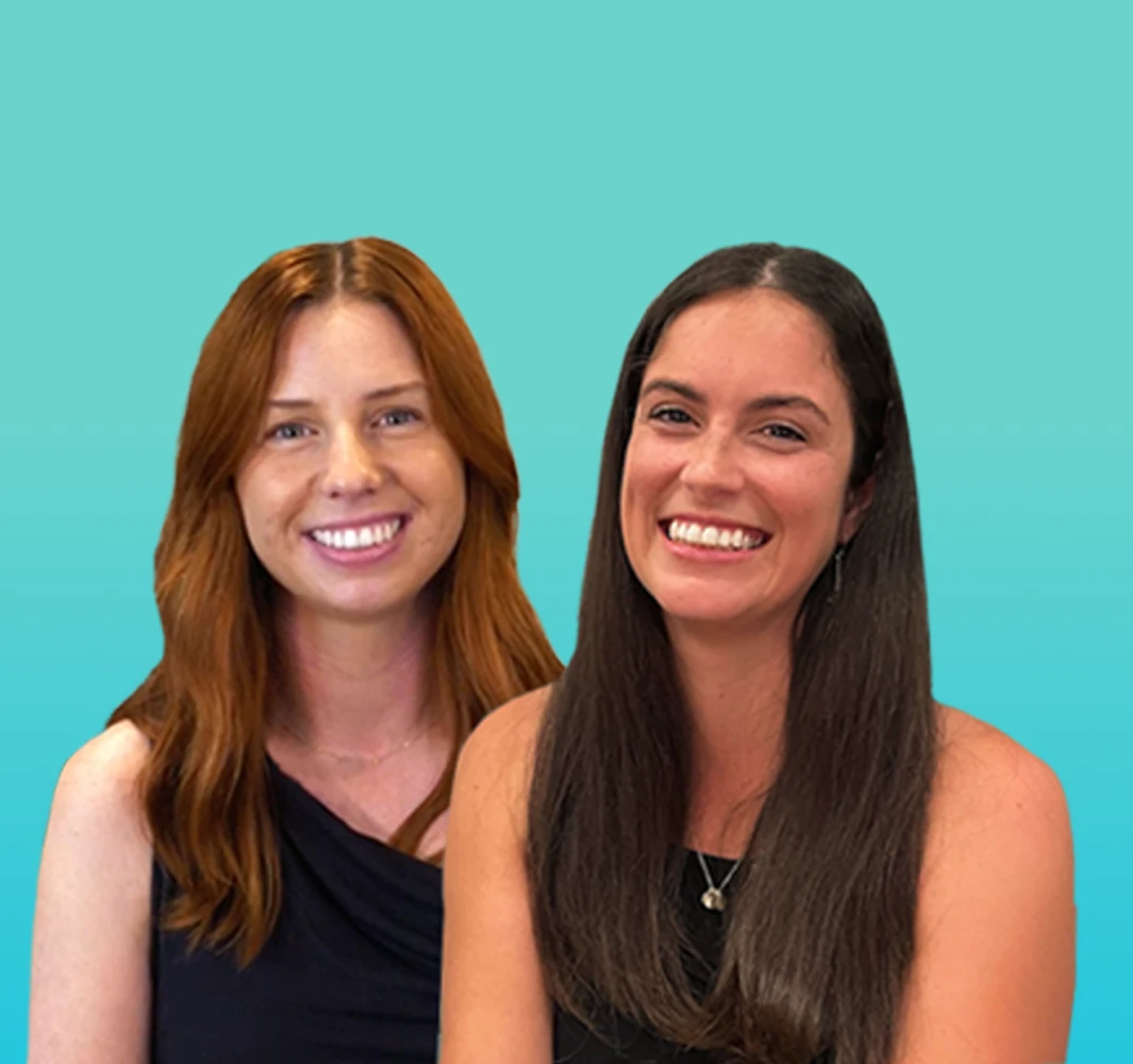 Two smiling women, one with red hair, one with dark, against a blue background, business or team portrait.