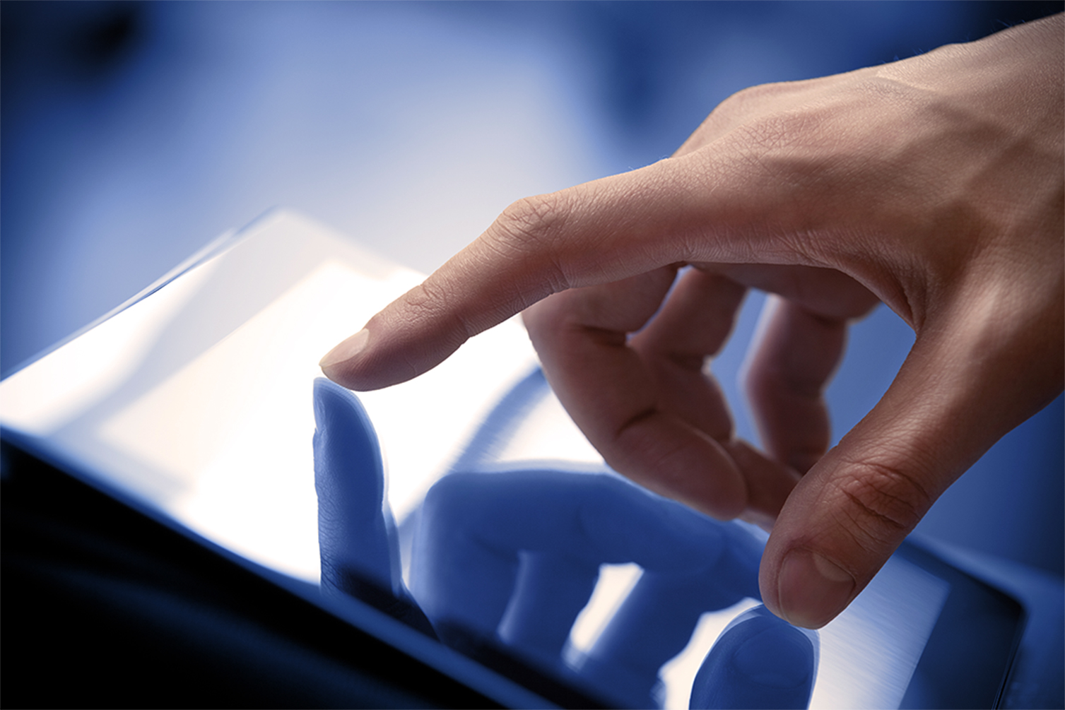Close-up of a hand with index finger touching a reflective touchscreen device.