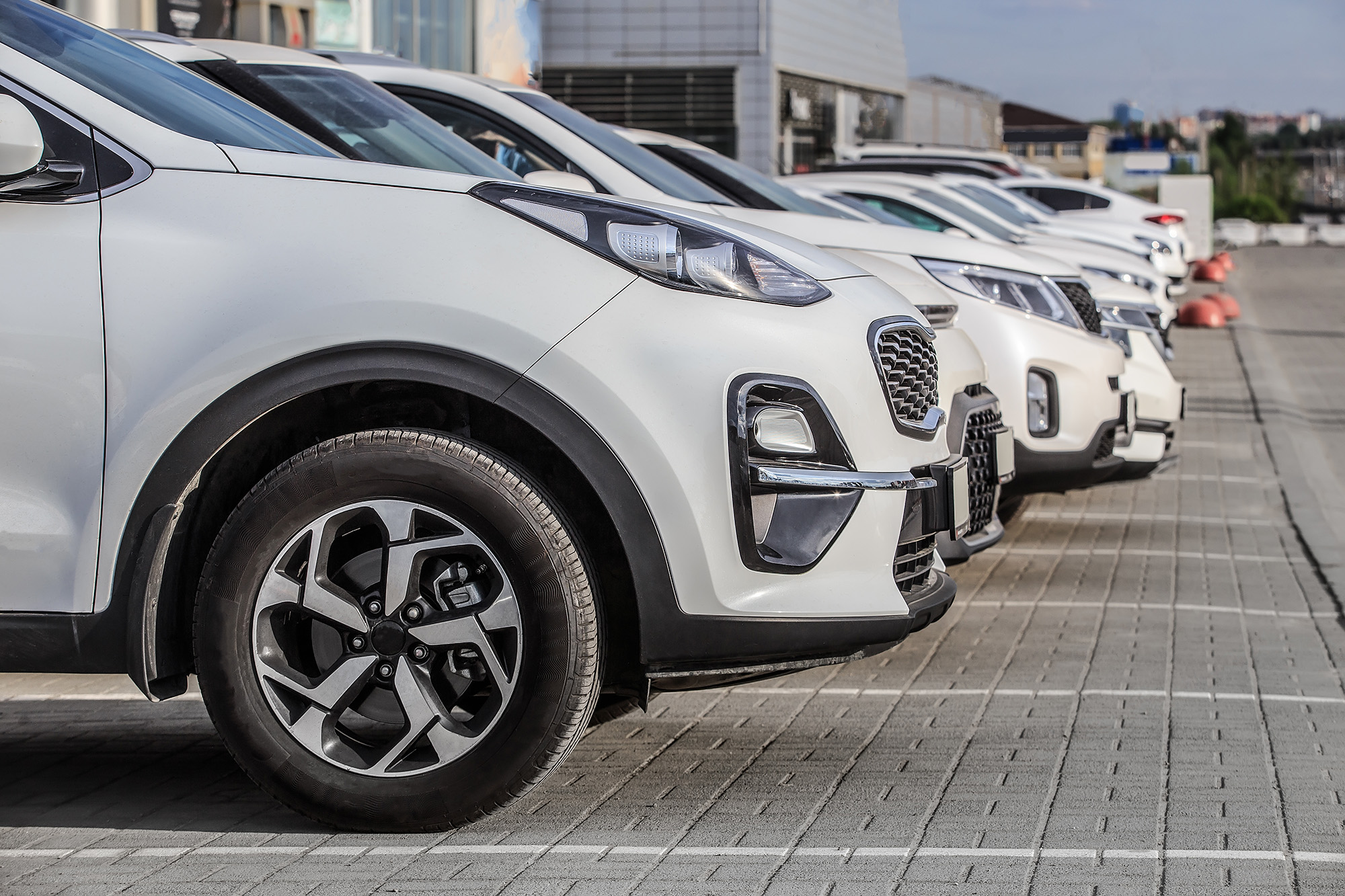 Row of white cars parked in an outdoor lot on a tiled surface under daylight.