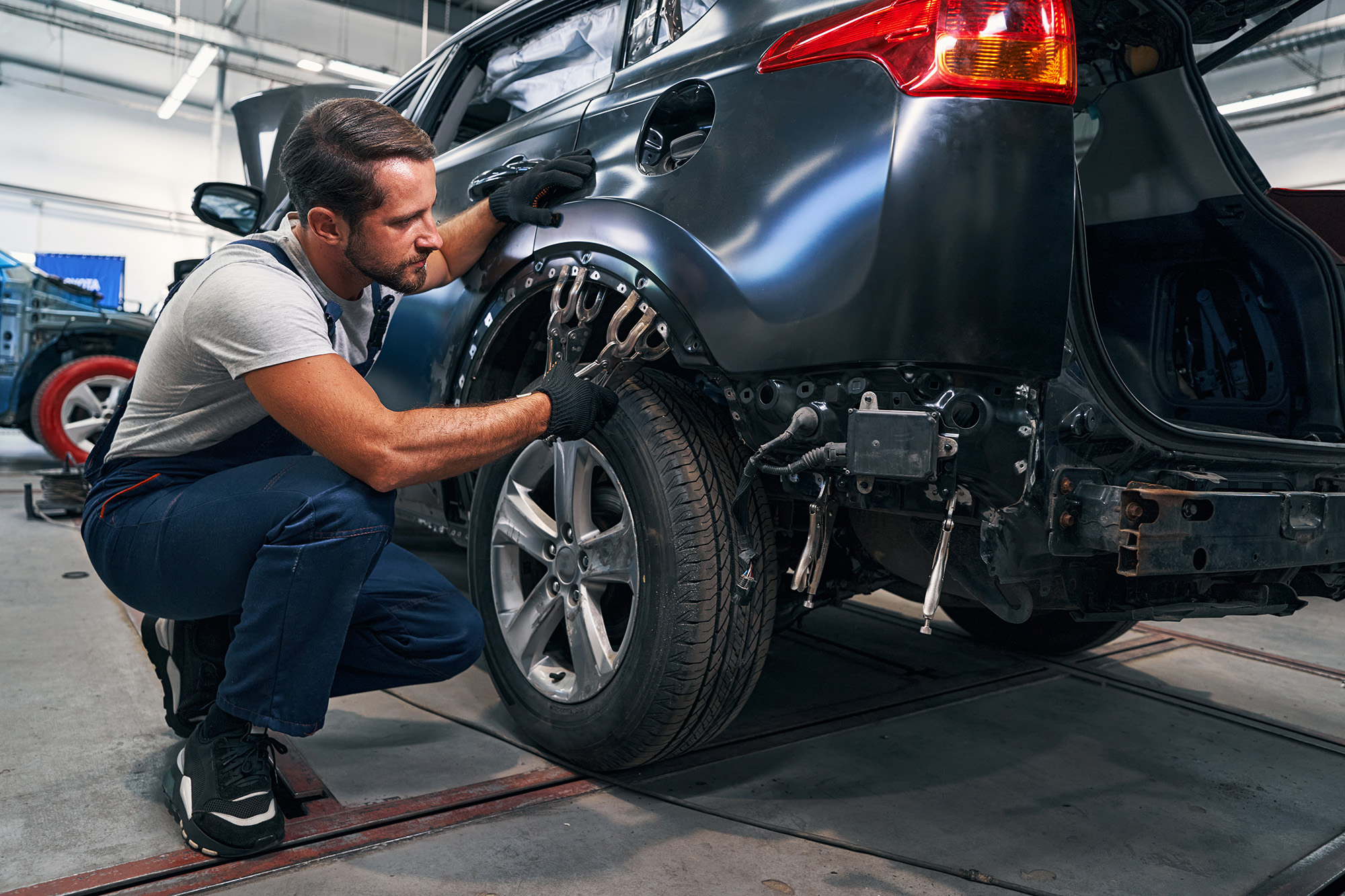 Mechanic in gloves repairing the rear side panel of a black car in a workshop.