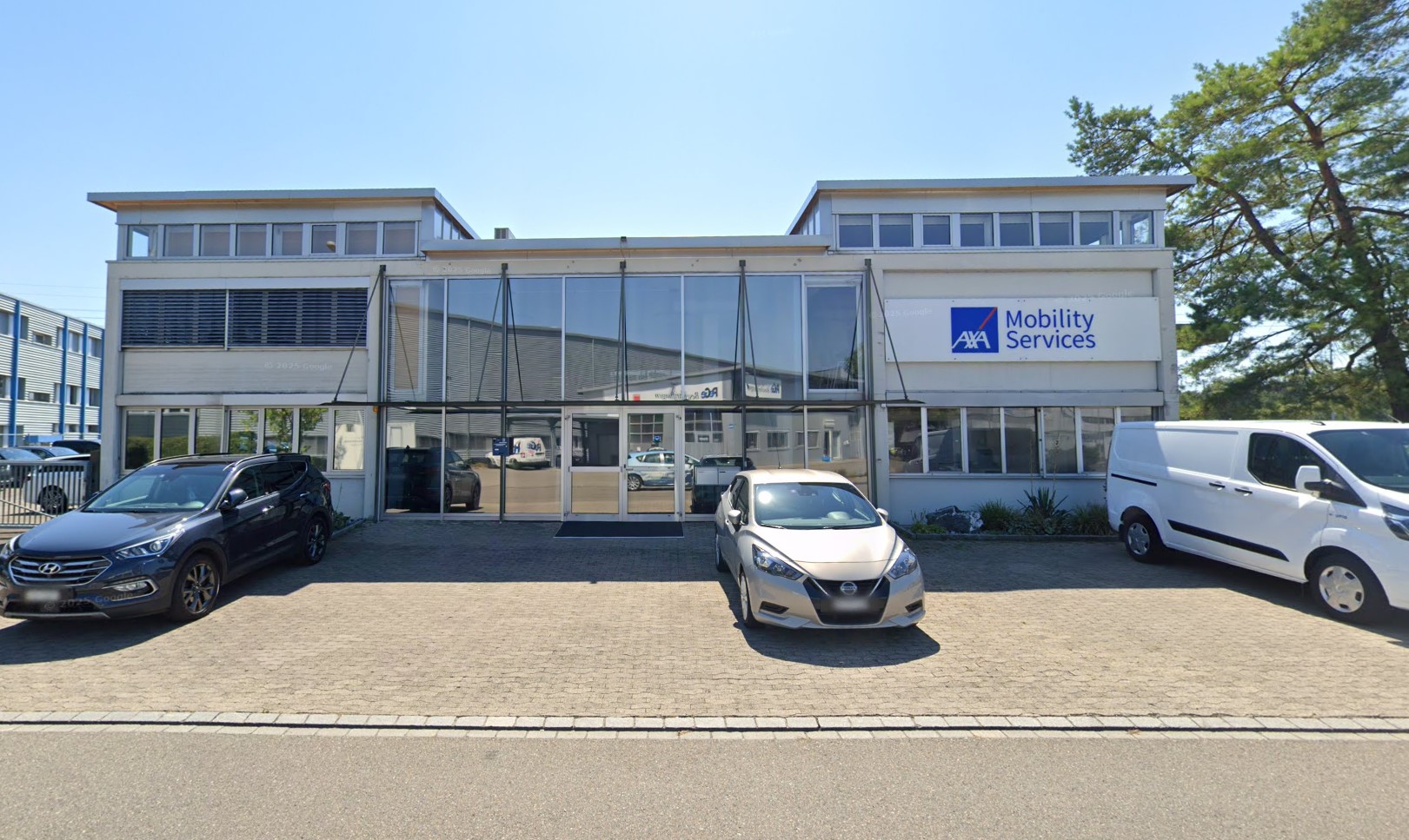 Modern office building with large glass entrance and AXA Mobility Services sign, with cars parked in front.