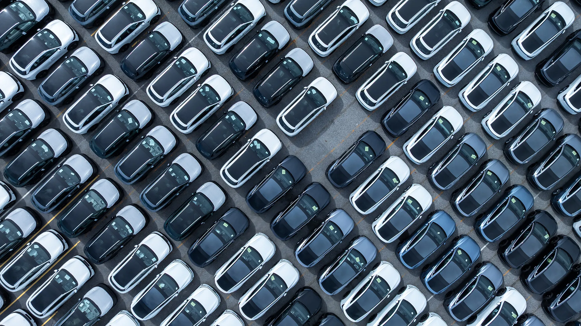 Aerial view of black and white cars neatly parked in rows in a large parking lot.