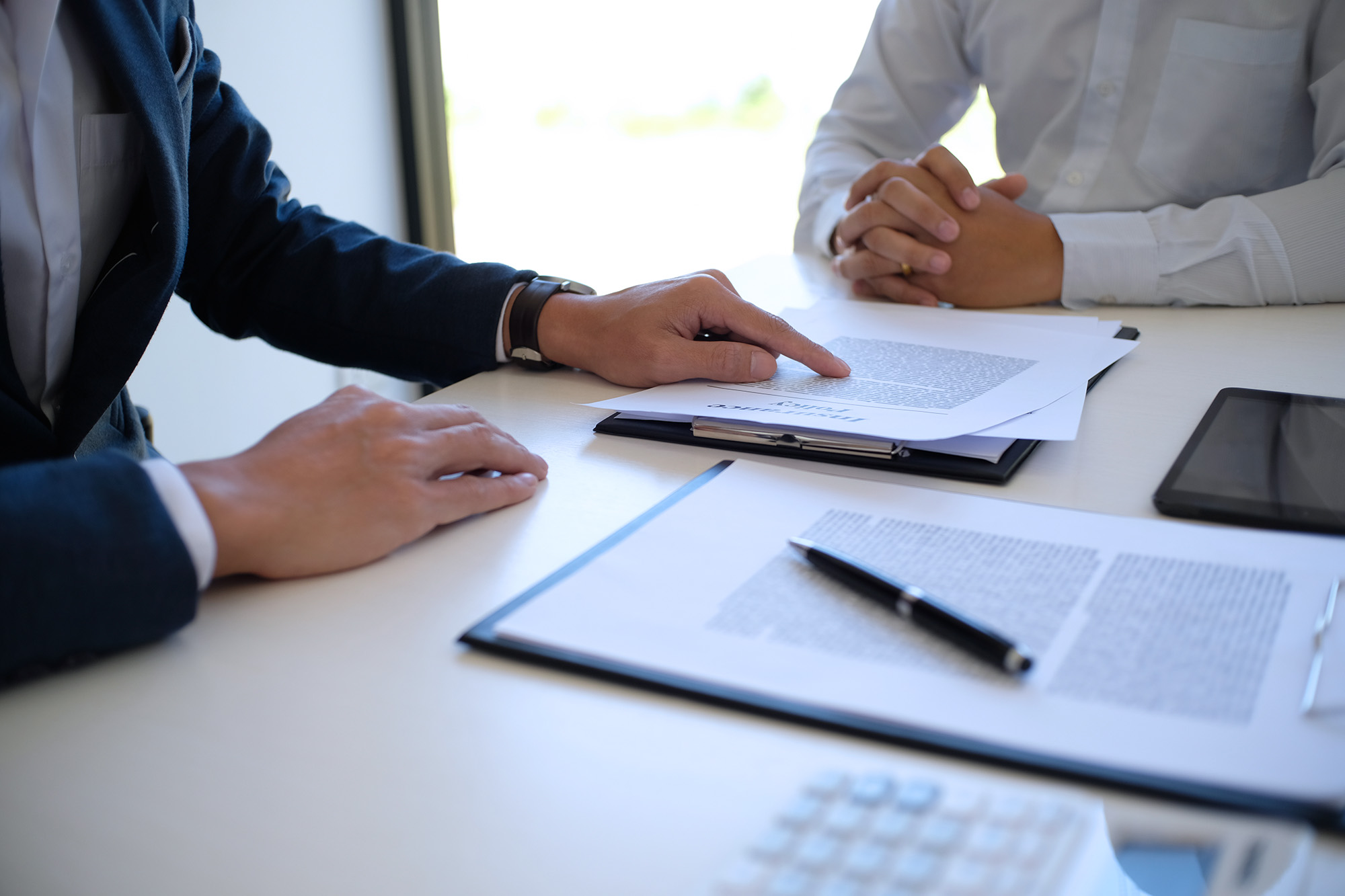Two people at a desk discussing printed documents, with one person pointing at a paper titled 'Insurance Policy'.