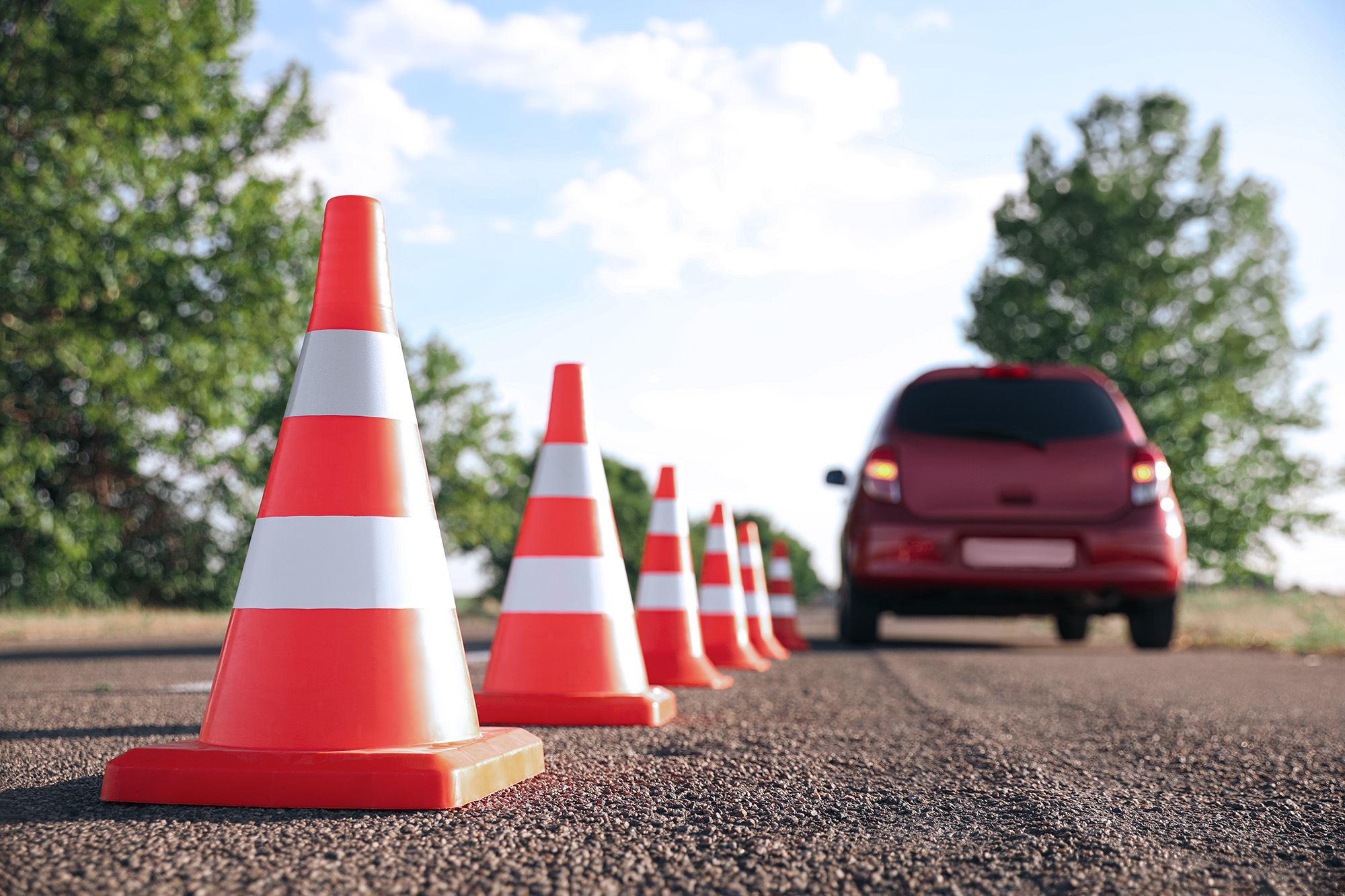 Row of orange traffic cones on asphalt road with a red car in the background during a driving safety training.