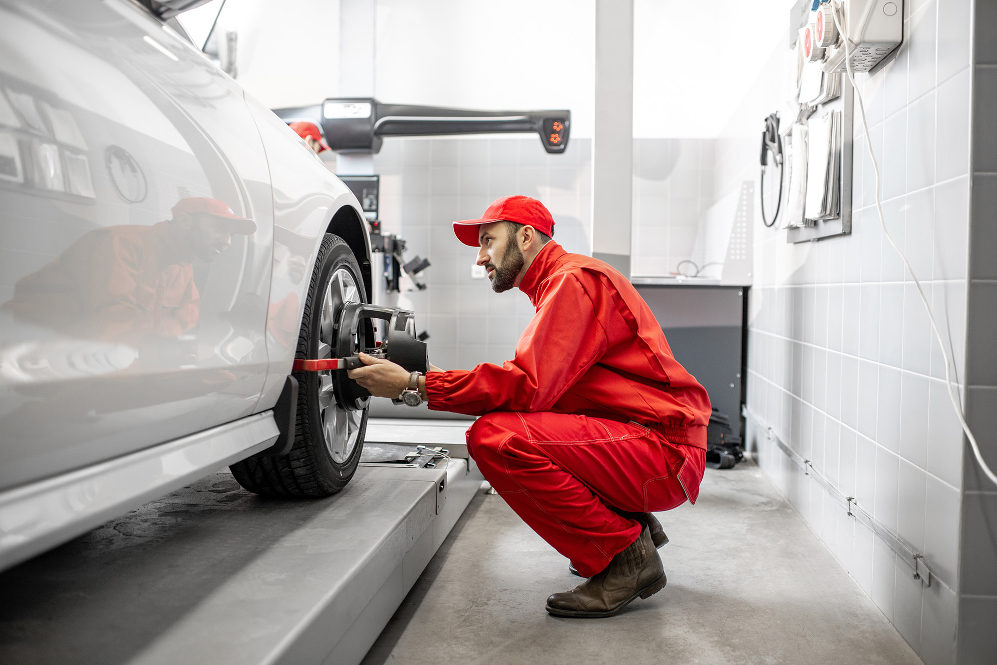 Mechanic in red uniform adjusting a sensor on a car's wheel during a wheel alignment service in a garage.