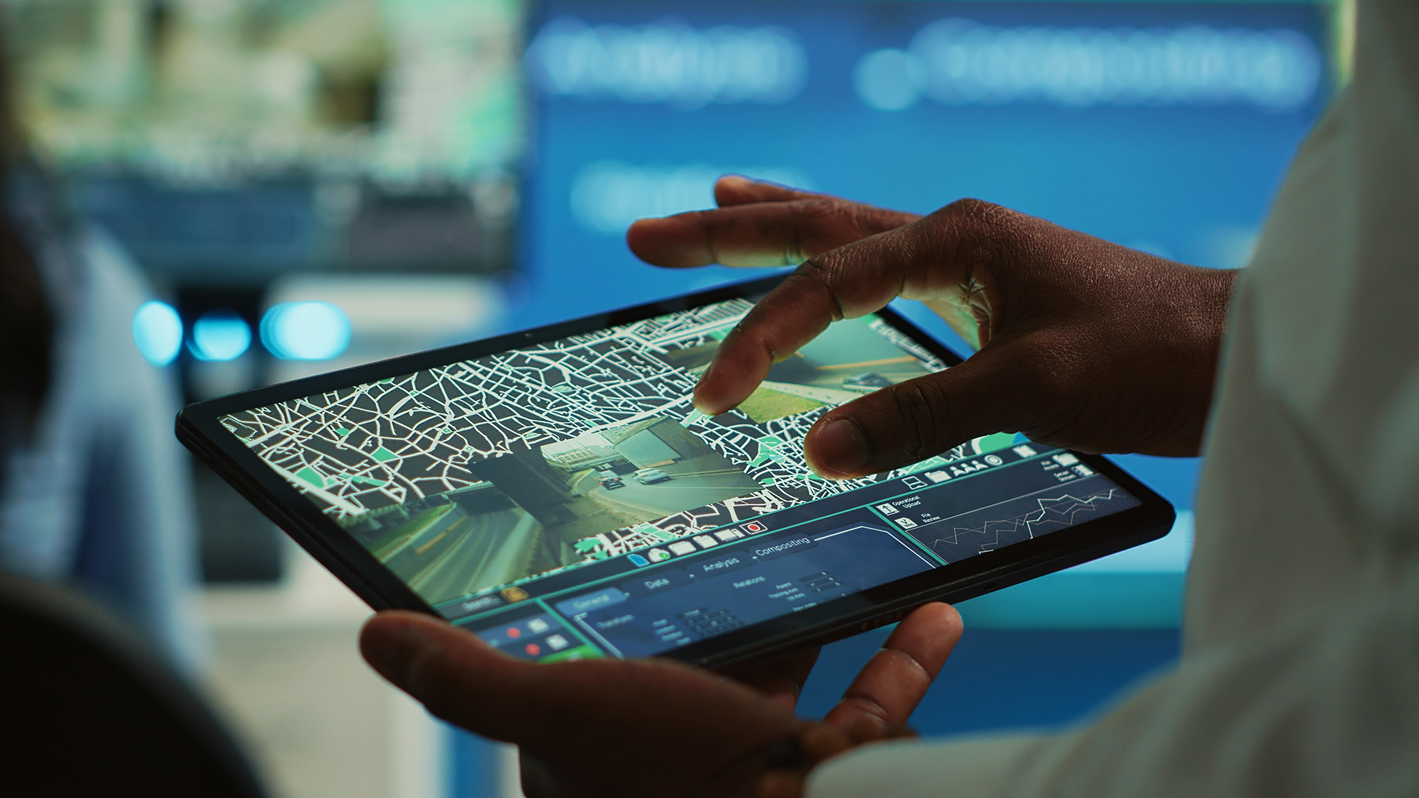 Close-up of hands interacting with a tablet displaying a digital map and live video feeds for geo tracking.